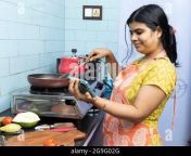 a pretty indian young woman wearing apron watching cooking video in smart phone in domestic kitchen on gas stove 2g9g02g.jpg from desi aunty in kitchen