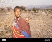 karatu tanzania october 16th 2022 a portrait of a masai woman in traditional clothes and jewelry carrying her baby on her back by her villages 2parep3.jpg from karatu her